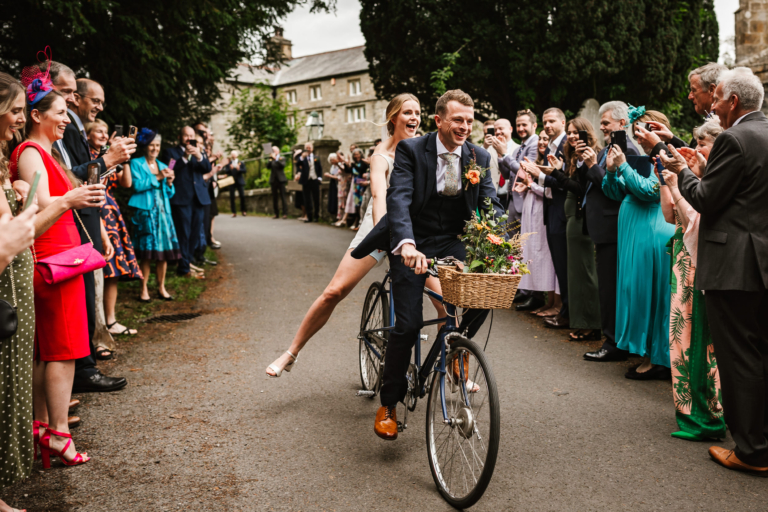 Bride and groom riding down the confetti line on a tandem bike