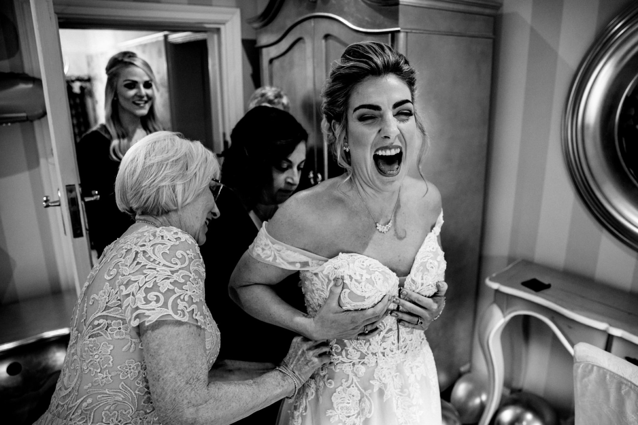 Bride laughing getting into her wedding dress at Eaves Hall